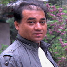 Ilham Tohti wearing a gray jacket with plants in the background.
