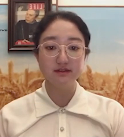 Li Qiaochu wearing glasses and a light top, delivering remarks to a camera.