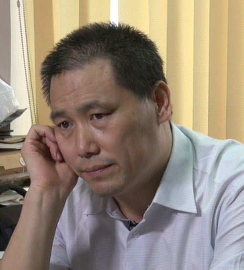 Pu Zhiqiang in a light shirt, with a hand beside his ear.