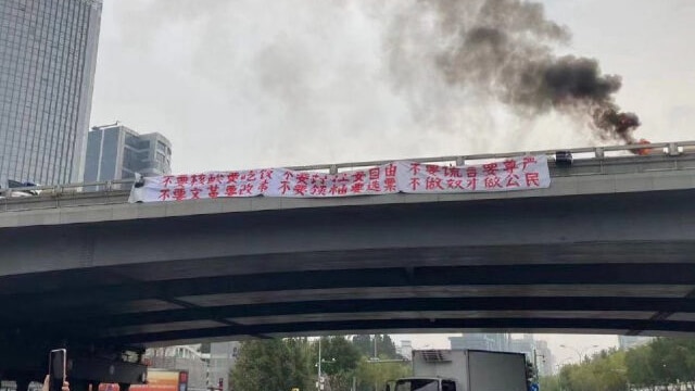 A white banner with red Chinese slogans hangs from Sitong Bridge, with smoke above it.