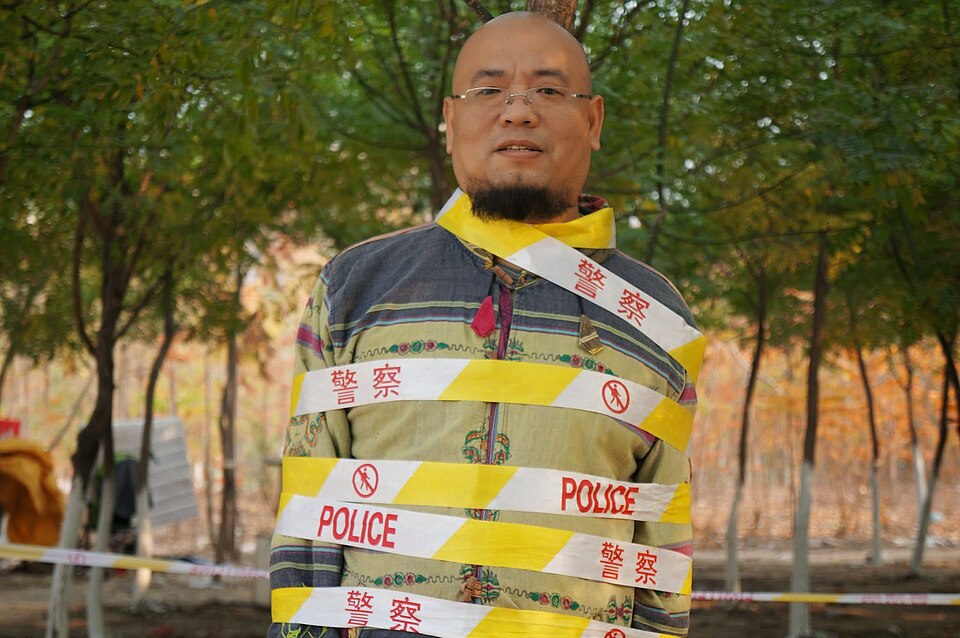 Wu Gan standing outdoors wrapped in police tape.